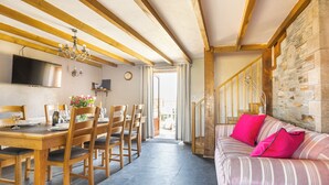 A dining area with a wooden table and chairs, a chandelier, and a stone wall. - Family cottage near the sea - Pet Friendly sleeps 6 - 5 mins from Port Isaac (Port Isaac)