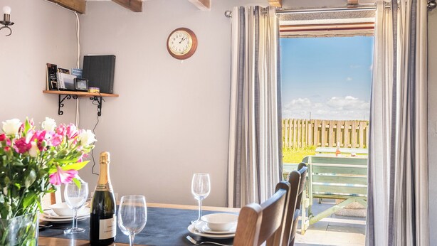 A dining area with a table set for two, a bottle of champagne, and a clock on the wall. - Family cottage near the sea - Pet Friendly sleeps 6 - 5 mins from Port Isaac (Port Isaac)