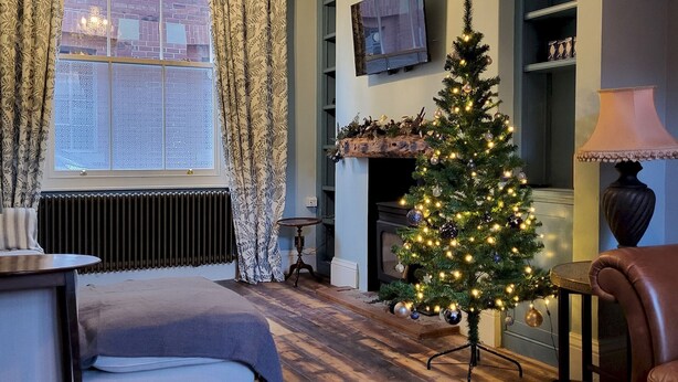 Un salon chaleureux avec une cheminée, un sapin de Noël et un téléviseur fixé au mur.