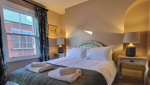 Une chambre d’hôtel avec un grand lit, deux tables de chevet avec des lampes, une fenêtre avec des rideaux et un tableau au mur.