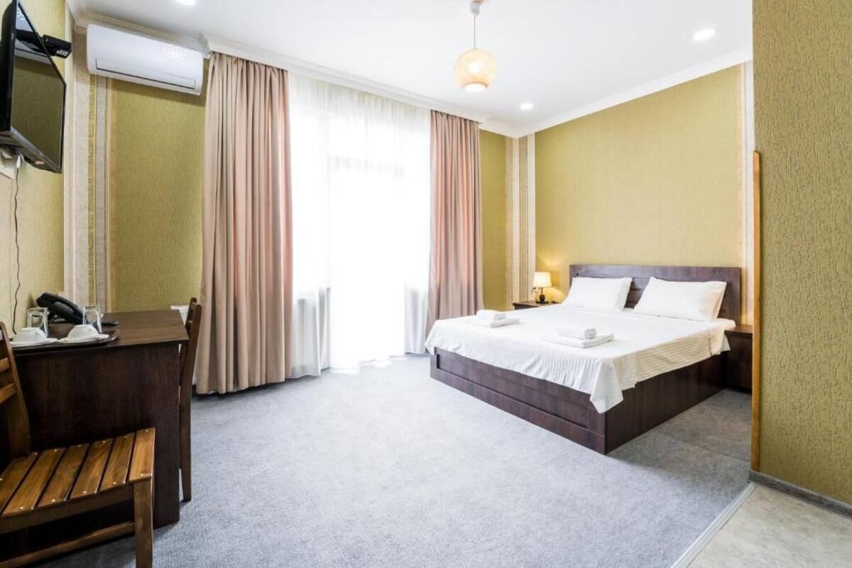 A hotel room with a bed, bedside table, lamp, and a desk with a chair.