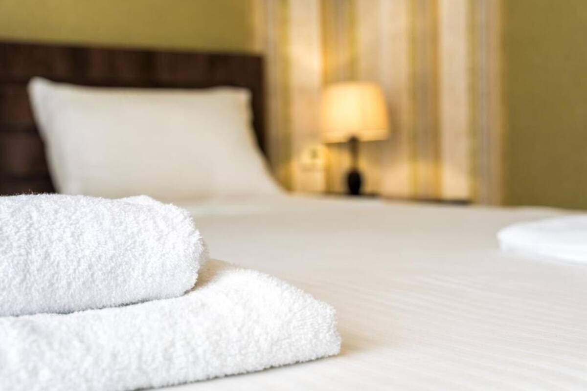 A neatly made bed with white linens and two folded towels in the foreground.