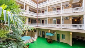 Et hotel med flere etager, altaner, indendørs planter og en grøn gårdhave.