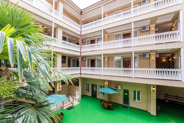 A multi-story hotel with balconies, indoor plants, and a green courtyard.