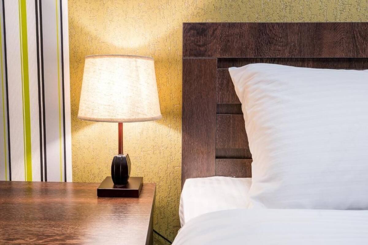 A hotel room with a wooden headboard, a bedside lamp, and a bed with white bedding.