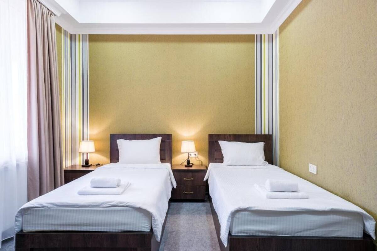 A hotel room with two beds, each with a nightstand, a lamp, and a folded towel.