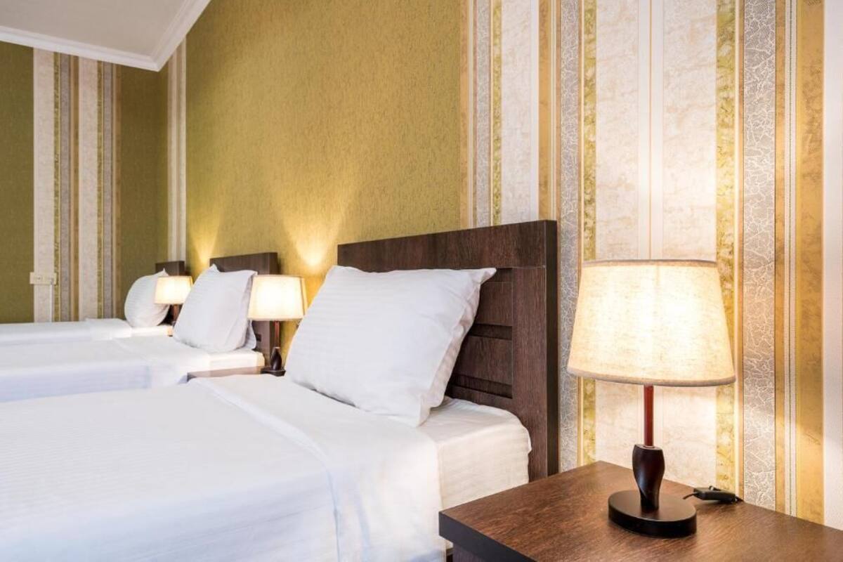 A hotel room with two beds, a wooden nightstand with a lamp, and striped wallpaper.