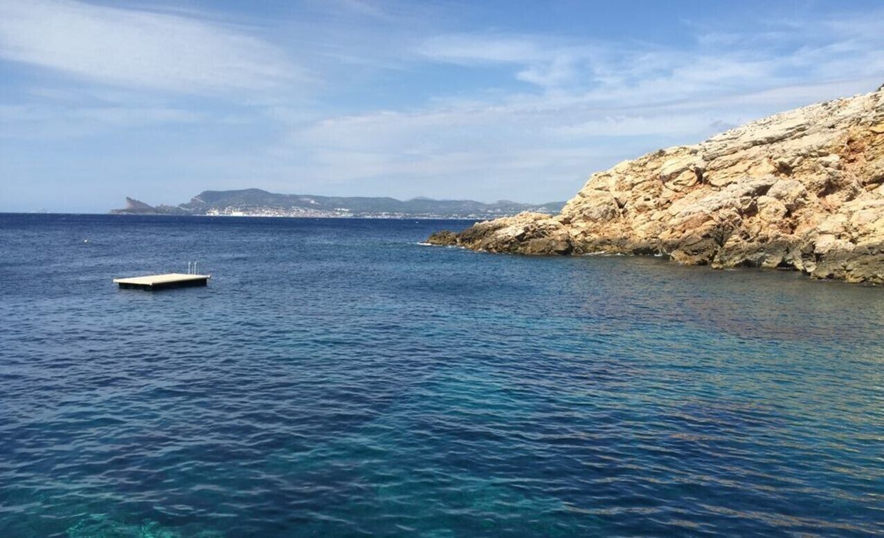 A coastal scene with clear blue waters, a rocky shoreline, and a small boat.