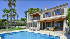 Une maison à deux étages avec une piscine, un espace salon extérieur et des palmiers.
