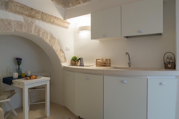 A compact kitchen with a stone arch, white cabinetry, a sink, and a small dining table with breakfast items. - Terrazza Blu Cobalto by Wonderful Italy (Ostuni)