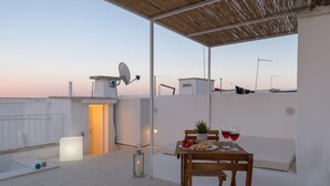 Terraço no telhado com uma mesa posta para dois, antena parabólica e vista para a paisagem urbana.