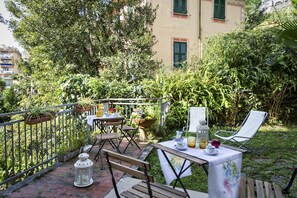 An outdoor patio with a table set for dining, surrounded by lush greenery and a stone wall.