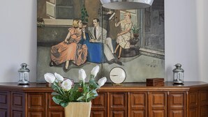 A vintage painting of a couple on a couch with a clock and two lanterns on a wooden cabinet. - Una Terrazza su Rapallo by Wonderful Italy (Rapallo)