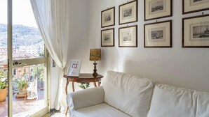 A room with a white sofa, a small table with a lamp, and a window with curtains. - Una Terrazza su Rapallo by Wonderful Italy (Rapallo)