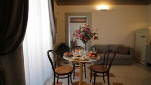 A dining area with a round table, four wicker chairs, a vase of flowers, and a sofa in the background.