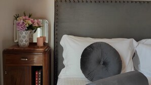 A neatly made bed with a grey headboard, a bedside table with a vase of flowers, and a wall-mounted light.