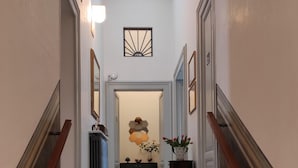 A hallway with a marble staircase, a radiator, a hexagonal wall decoration, and a vase with flowers.