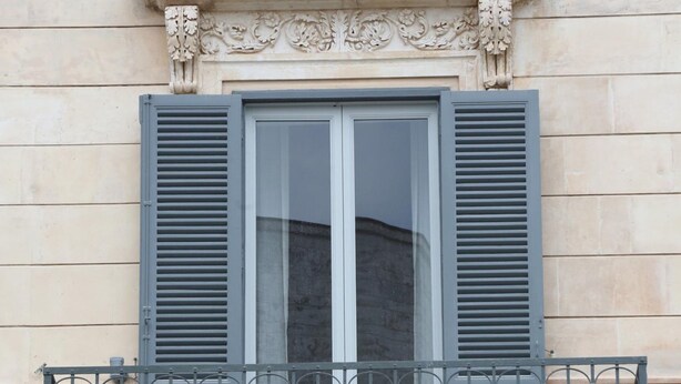 A building facade with a window featuring a balcony with a wrought iron railing.