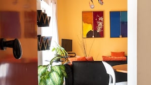 A room with a wooden ceiling, a black sofa, a white chair, and a patterned floor. - Iconic Apt in Porta Carini by Wonderful Italy (Palermo)
