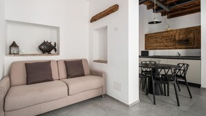 A modern living room with a beige sofa, a dining area with black chairs and a wooden table, and a kitchen with wooden cabinets and a hanging light fixture. - San Michele Apartments - Lignum by Wonderful Italy (Bologna)