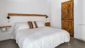 A bedroom with a bed, a wooden headboard, a bedside table, a nightstand, a wall-mounted lamp, and a wooden door. - San Michele Apartments - Lignum by Wonderful Italy (Bologna)
