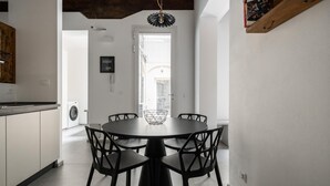 A modern kitchen with a built-in washing machine, a dining area with a round table and black chairs, and a wooden shelf with books. - San Michele Apartments - Lignum by Wonderful Italy (Bologna)