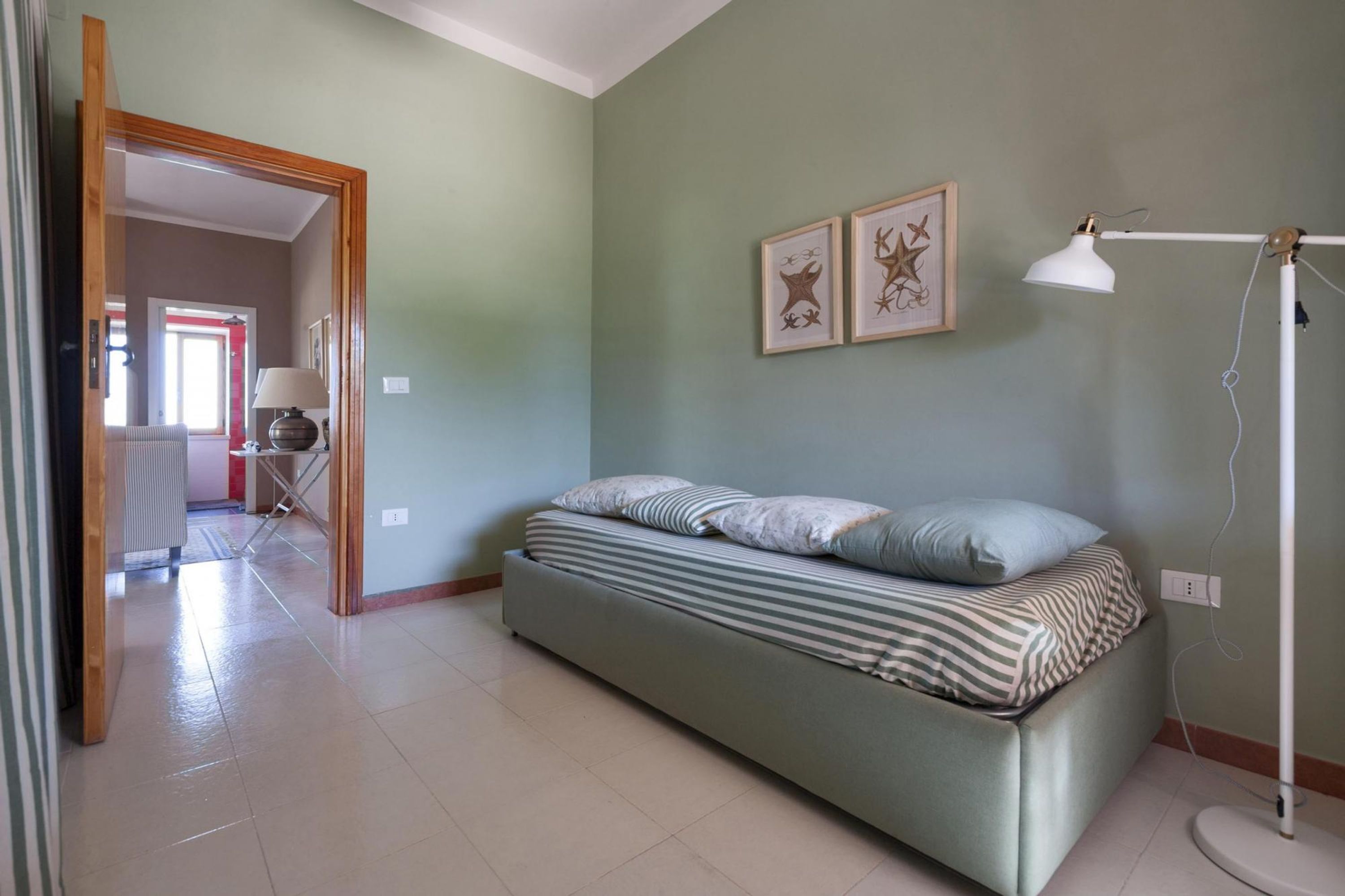 A bedroom with a bed, a standing lamp, and two framed pictures on the wall.