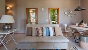 A cozy living room with a striped sofa, a dining table with chairs, a lamp, and a kitchen visible through an open door. - Villetta Tisbe by Wonderful Italy (Ostuni)