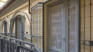 Une façade d’immeuble avec un balcon, une grande porte dotée d’un panneau de verre et une fenêtre ornée d’une grille métallique.