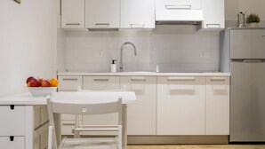 Une cuisine moderne avec des meubles blancs, un réfrigérateur en acier inoxydable et un plancher en bois.