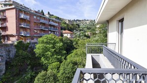 Ein Balkon mit Metallgeländer, der auf einen Hügel mit Gebäuden und Grünblick bietet.