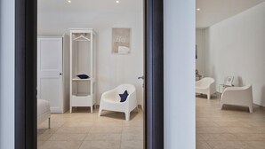 Ein modernes Badezimmer mit weißem Waschtisch, einem Sessel und einer Wandablage.