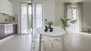 Eine moderne Küche mit weißen Schränken, einem eingebauten Ofen und einem Essbereich mit rundem Tisch und transparenten Stühlen.