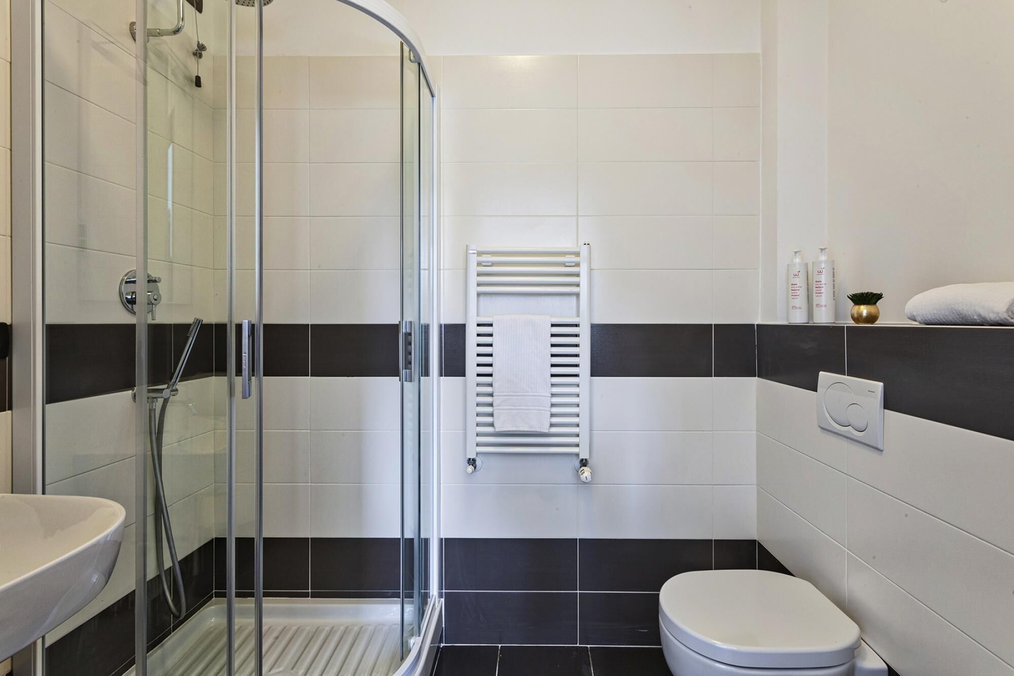 Ein modernes Badezimmer mit Duschkabine aus Glas, einem weißen Waschbecken, einer Toilette und einem Handtuchhalter.