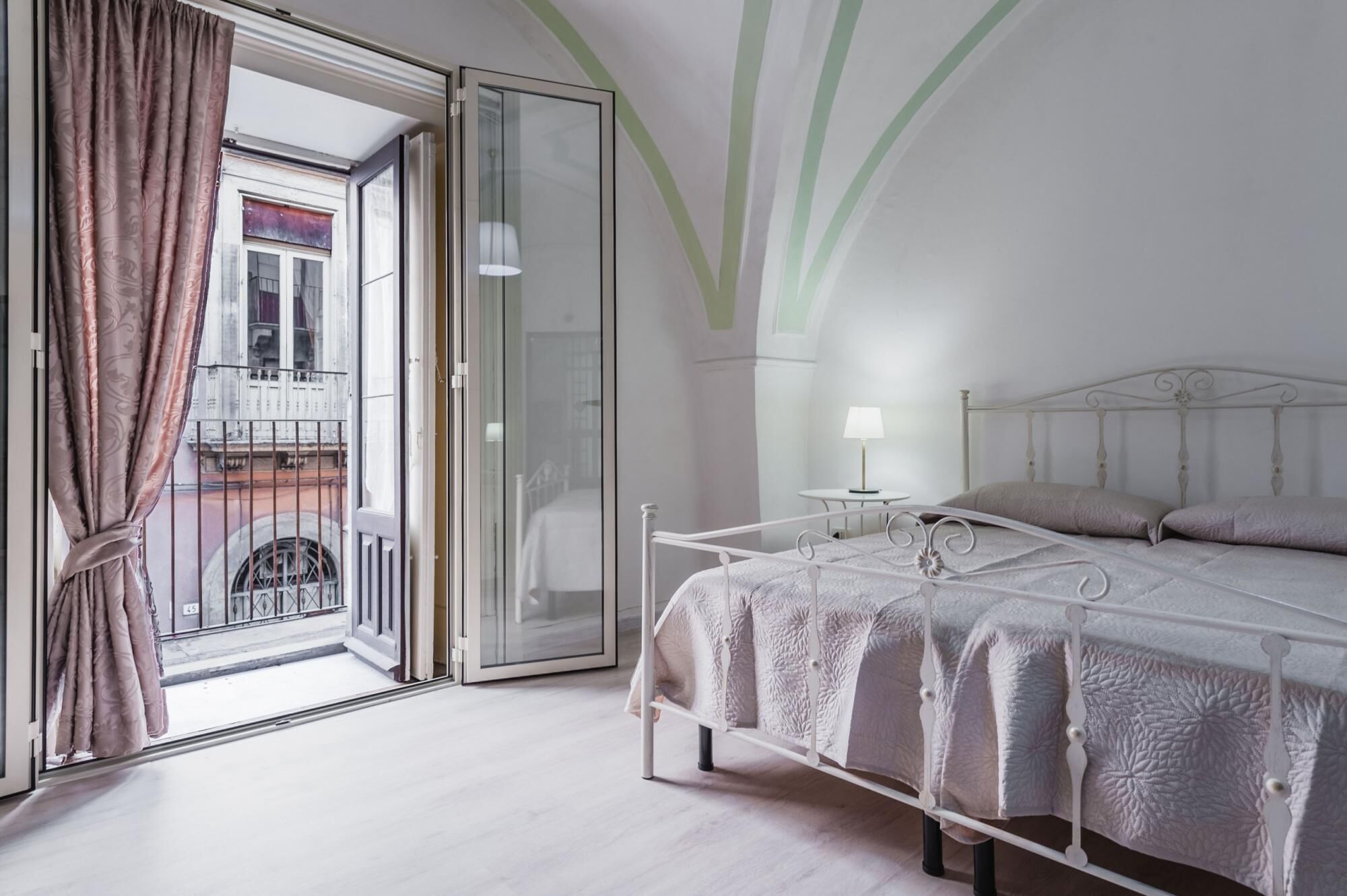 Un dormitorio con cama, mesita de noche, lámpara y vistas al balcón exterior.