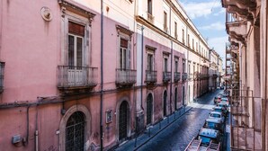 A narrow street lined with pink buildings, featuring balconies and arched windows. - Apartment Manzoni 40 by Wonderful Italy (Catania)