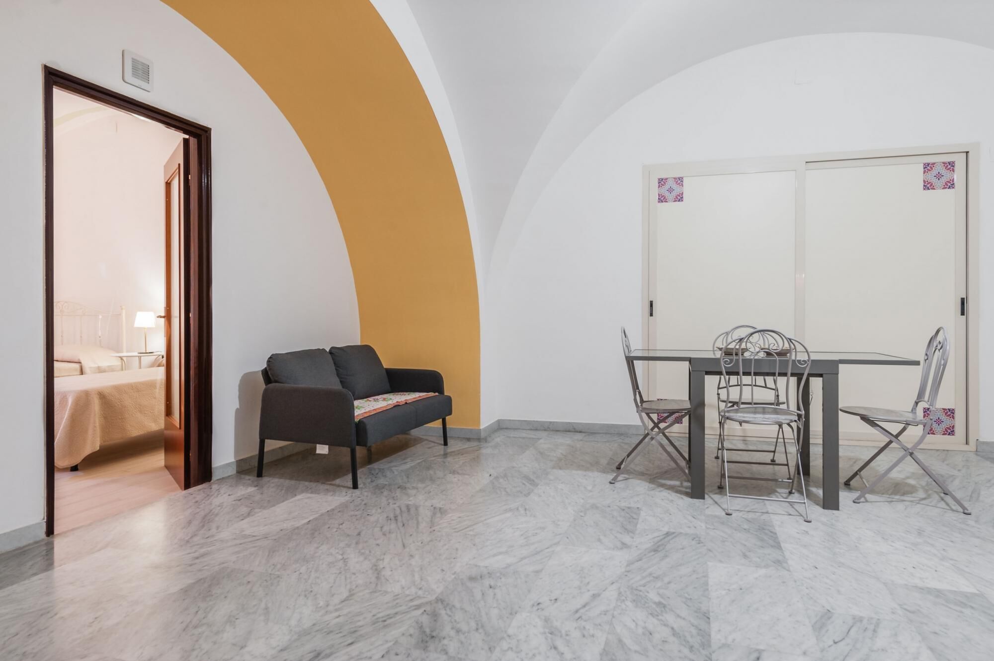 A room with a sofa, a dining table with chairs, and a door leading to another room.