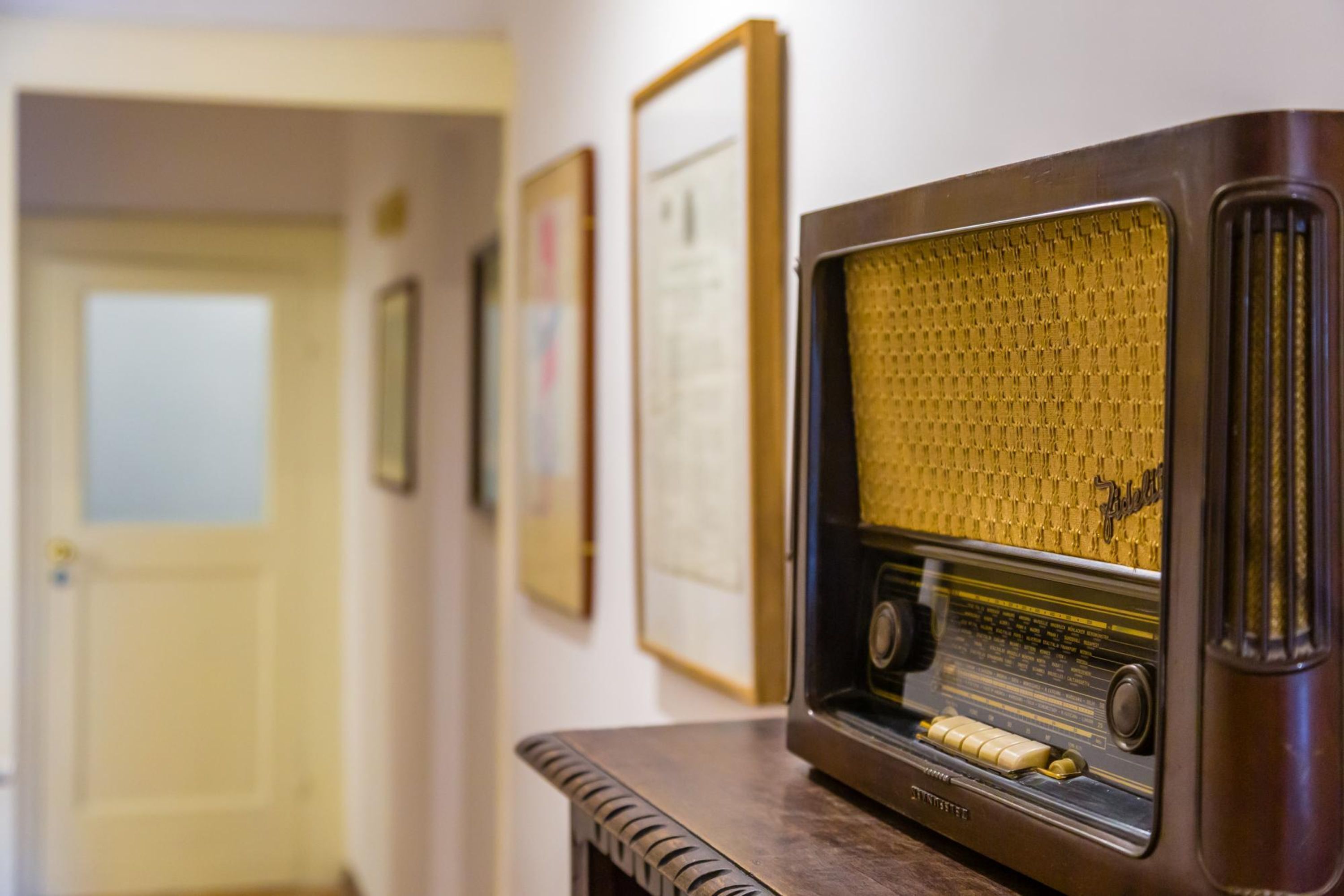 A vintage radio on a wooden table in a hallway with framed pictures on the wall.