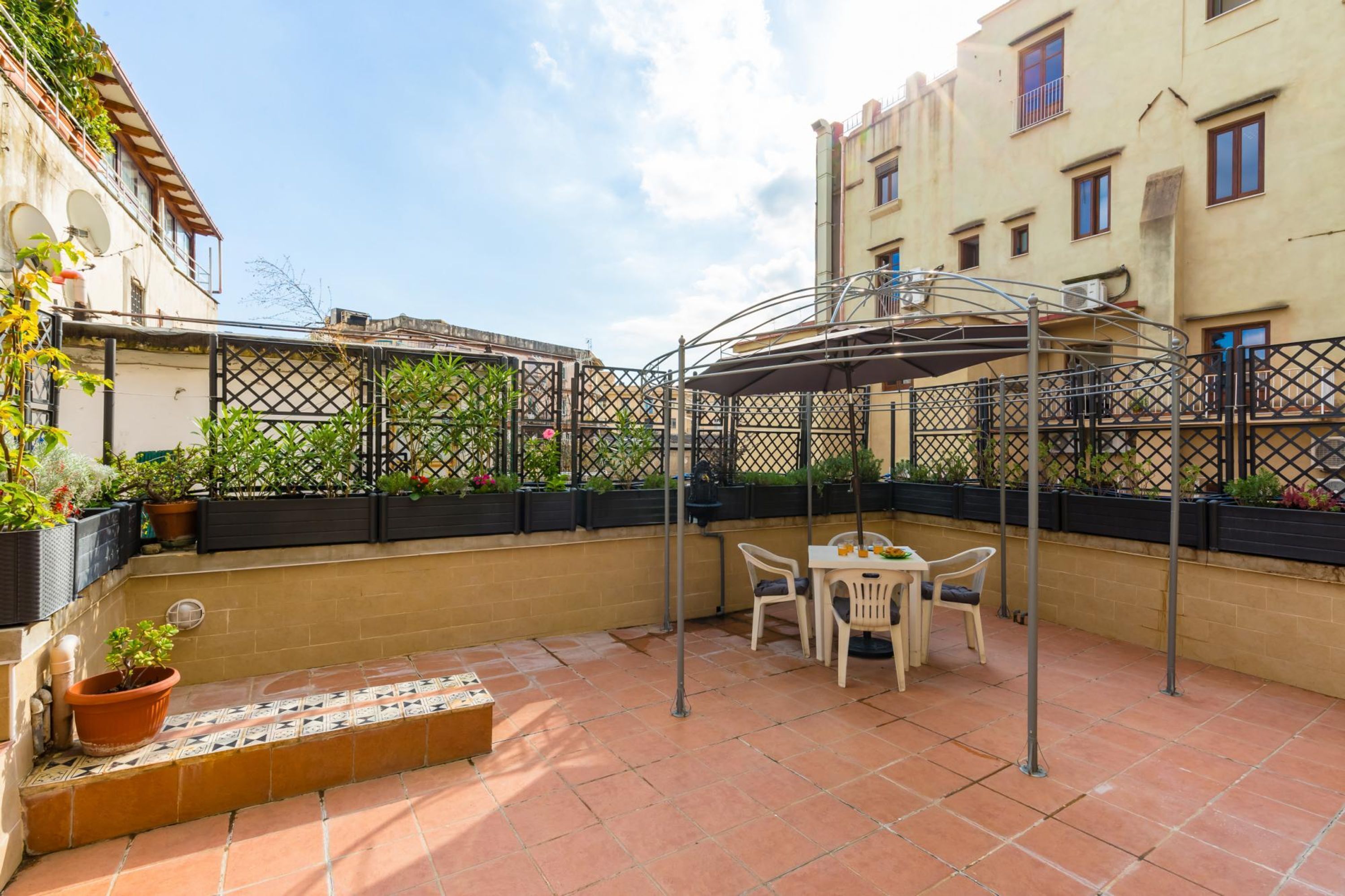 Un patio con una mesa y sillas, rodeado por una cerca de metal y plantas en macetas.