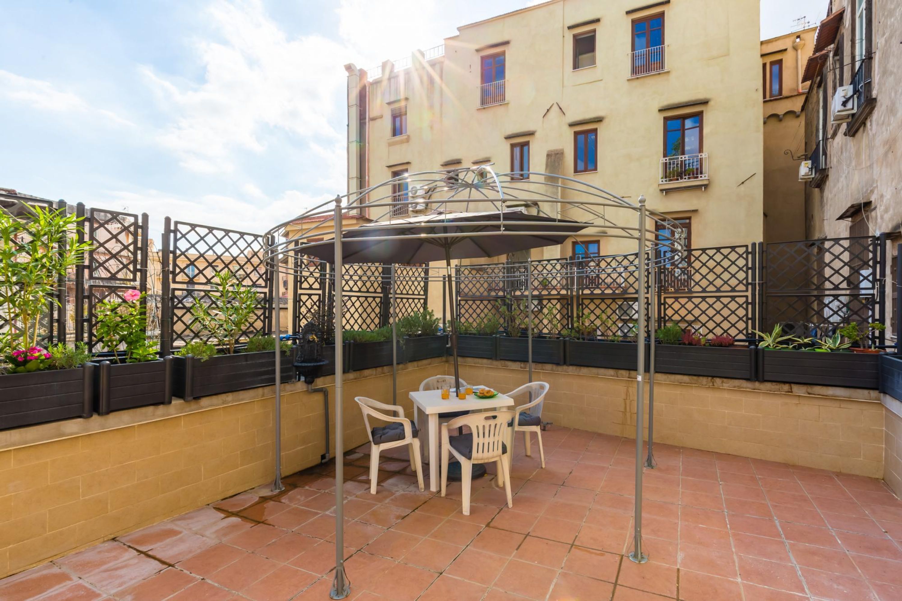 Una terrazza con tavolo e sedie, circondata da una recinzione in metallo e vasi di piante.