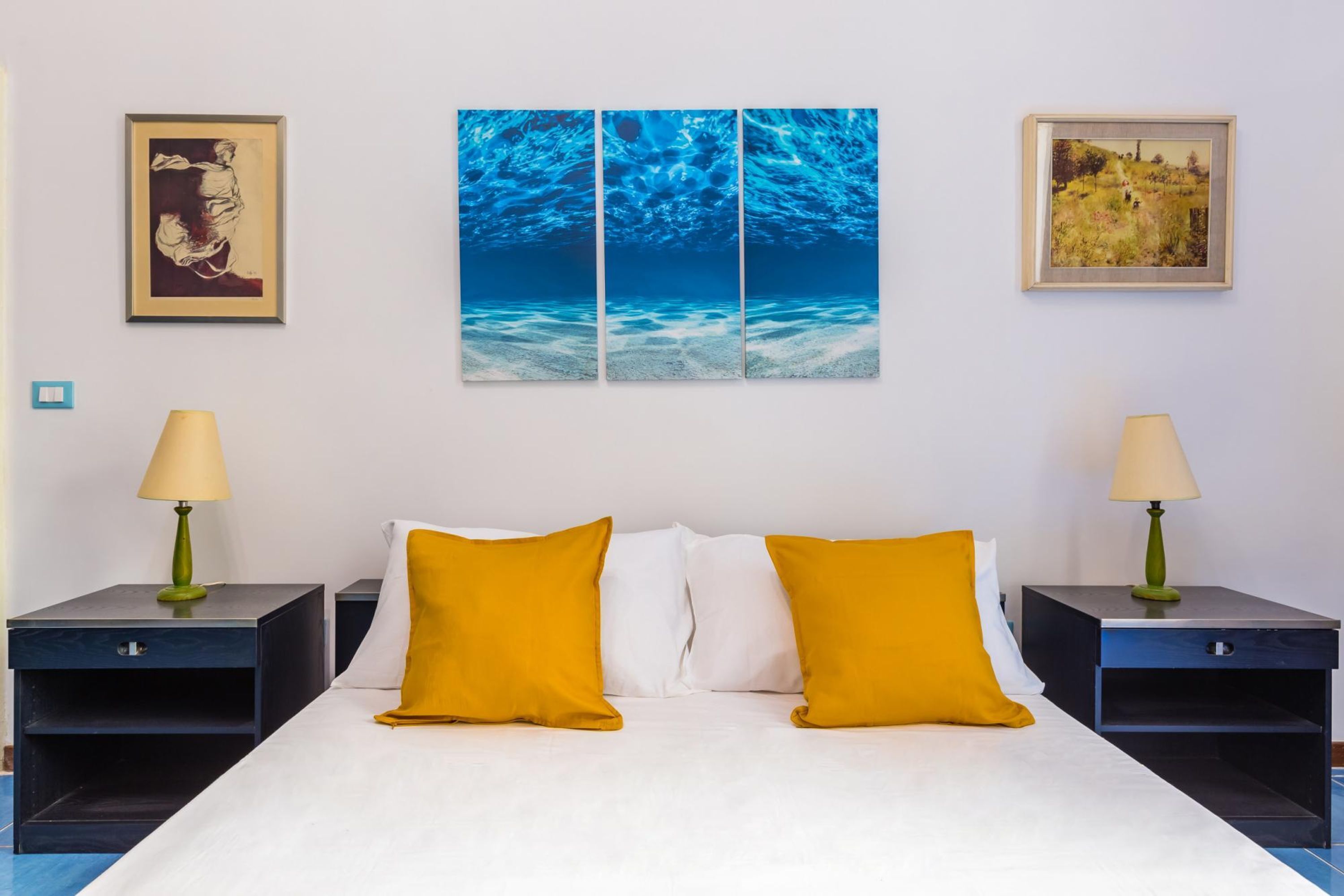 A hotel room with a bed, two nightstands, two lamps, and three paintings on the wall.