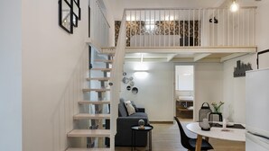 Eine moderne Wohnung mit einer Treppe, die zu einem Schlafzimmer auf dem Dachboden führt, einem Essbereich mit einem runden Tisch und einer im Hintergrund sichtbaren Küche.