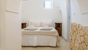 A bedroom with a bed, two bedside tables, a window, and a stone wall. - Villa d Itria Trullo Pool by Wonderful Italy (Ostuni)