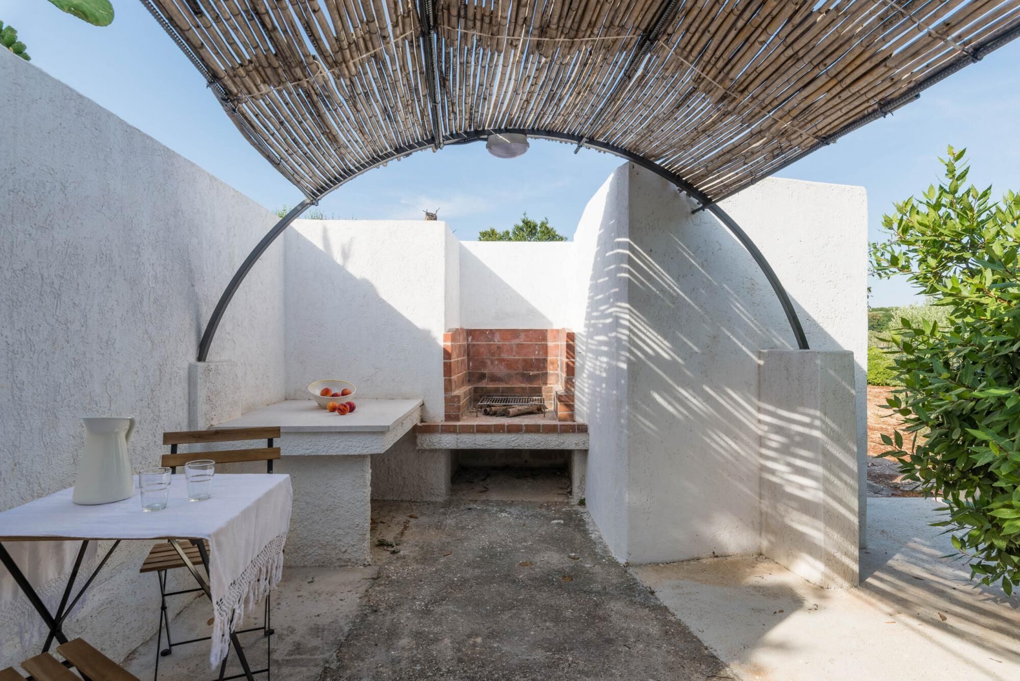 A small outdoor kitchen area with a brick oven, a table with a white tablecloth, and a chair.