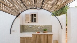 A small, enclosed outdoor kitchen area with a sink, a window with shutters, and a bamboo overhead structure. - Villa d Itria Trullo Pool by Wonderful Italy (Ostuni)