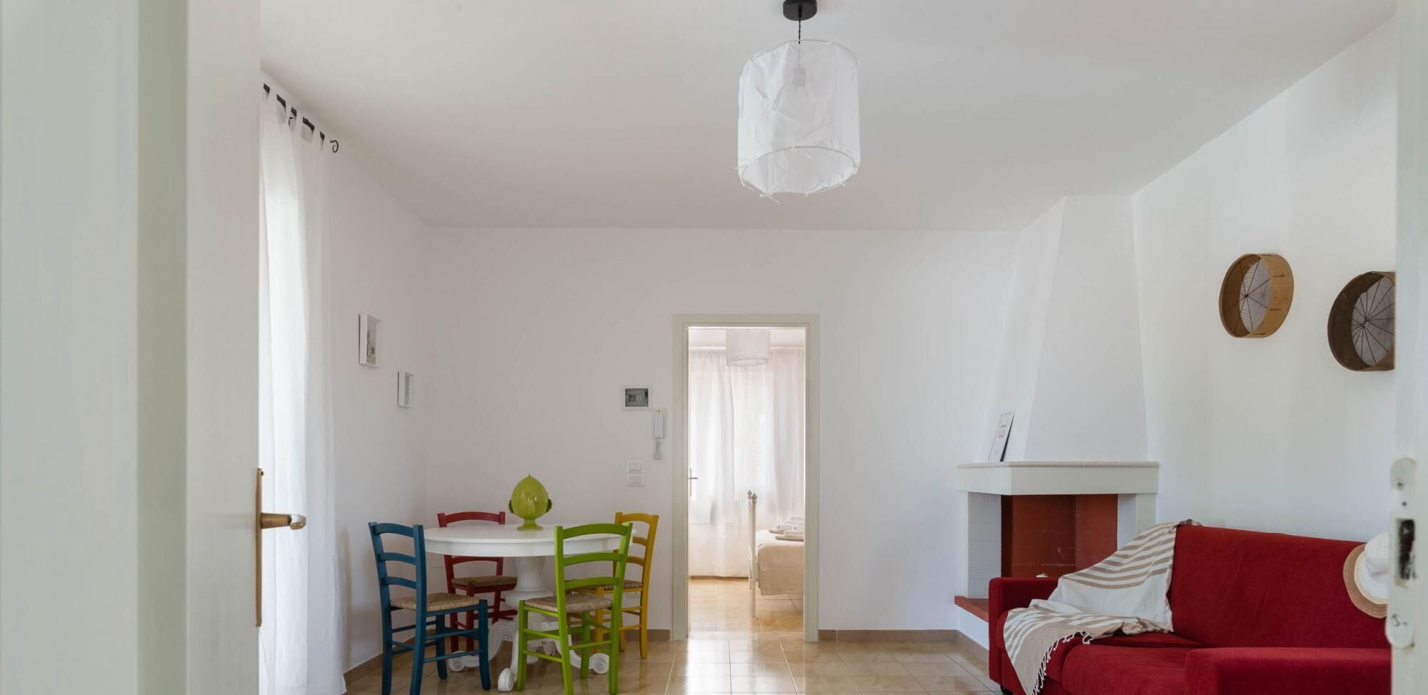 Una sala de estar con un sofá rojo, una mesa de comedor con sillas coloridas y una lámpara de techo blanca.
