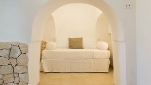 A cozy room with a stone wall, a white bed with pillows, and an arched ceiling. - Villa d Itria Trullo Pool by Wonderful Italy (Ostuni)