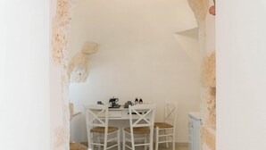 A small, white-walled room with a table and four chairs, a coffee machine, and a refrigerator. - Villa d Itria Trullo Pool by Wonderful Italy (Ostuni)