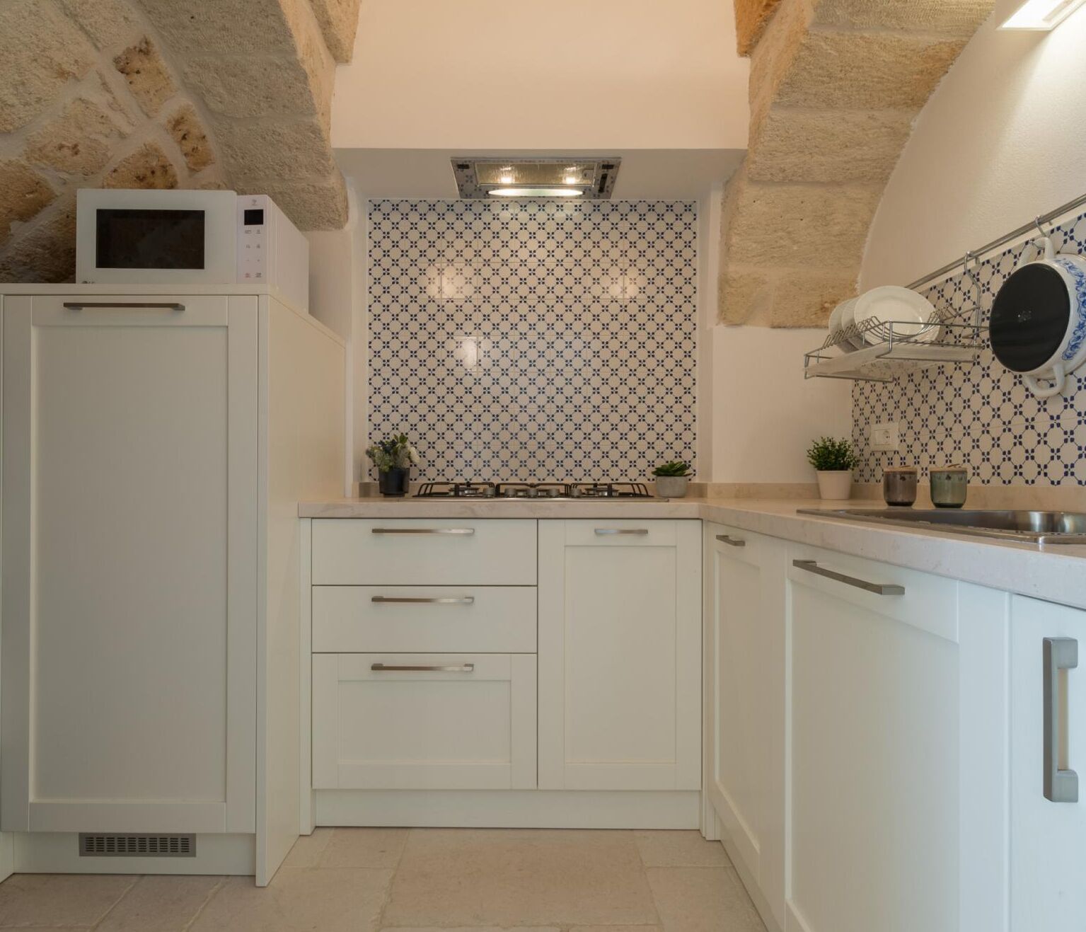 Une cuisine de taille réduite, avec des meubles blancs, un four à micro-ondes, une cuisinière à gaz et un évier.