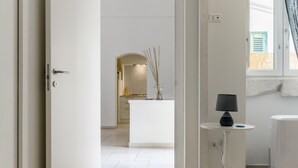A modern interior with a white door, a small table with a lamp, and a view of a kitchen area. - Casetta Biancapietra by Wonderful Italy (Ostuni)